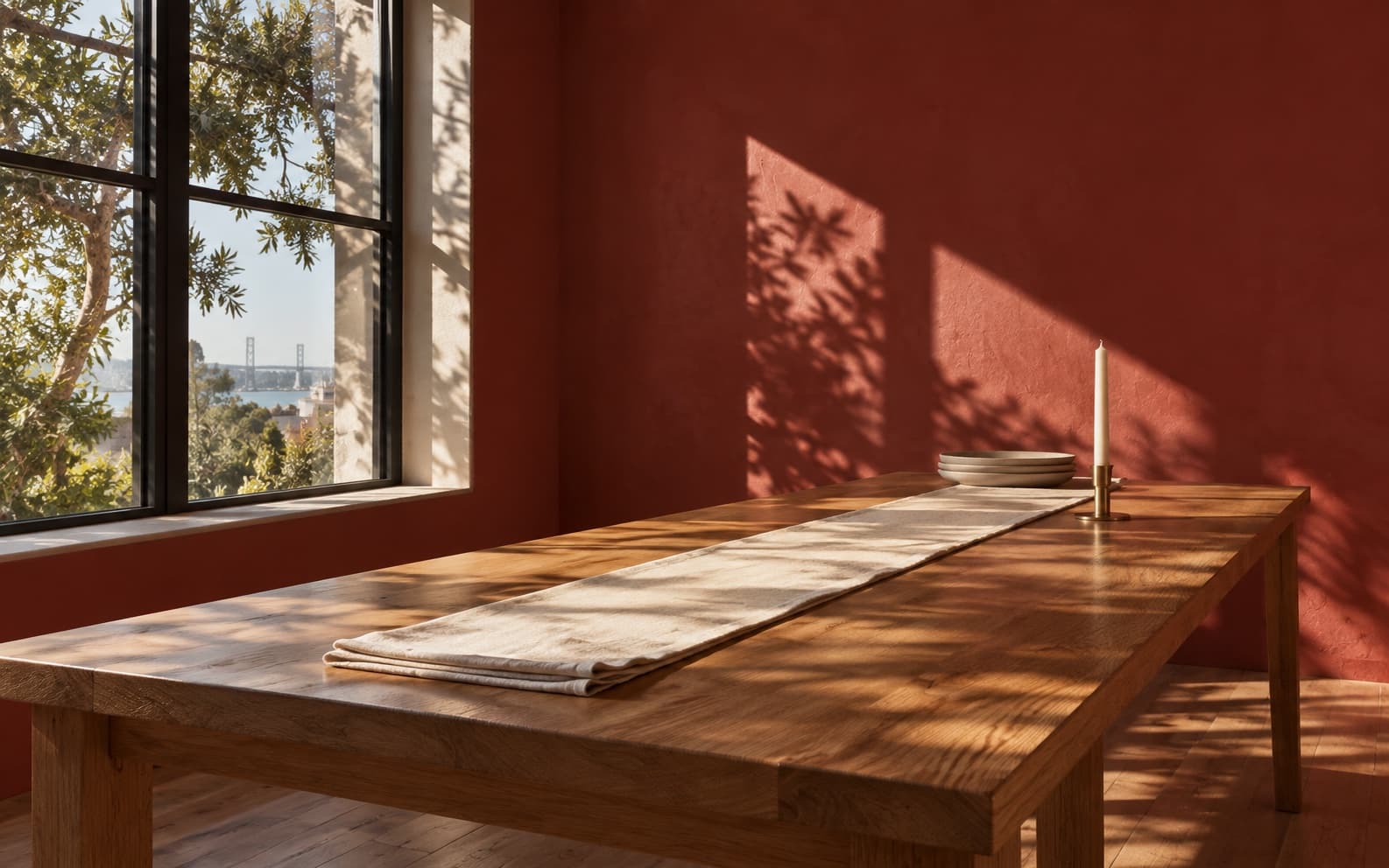A long bare table in an empty red-walled room in late light.